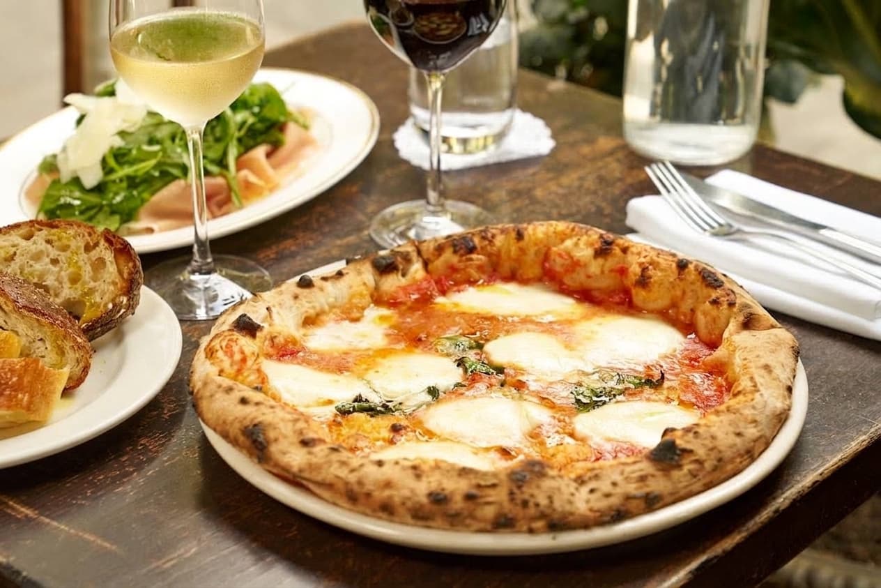 Pizza and glasses of wine on a sunlit restaurant table